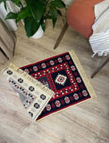 Two patterned Armenian ethnic rugs on a wooden floor with a plant and chair in the background.