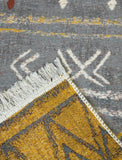 Close-up of a textured yellow and gray rug with geometric pattern and fringes.