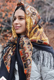 A woman wearing a brown and orange floral patterned scarf with fringe, styled as a shawl over the shoulders.