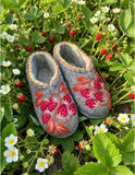 Woolen clogs loafers for house made of natural thick wool and with wild strawberry embroidery on a green grass in a nature.