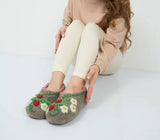Person wearing cozy woolen slippers with floral and berry design on a light background
