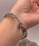 Silver bracelet with a charm on a wrist against a neutral background