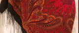 Close-up of a red and gold paisley patterned shawl with black fringe.