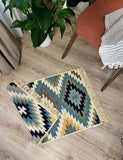 Geometric patterned yellow and green rug on a wooden floor with a plant and chair in the background