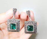 A set consisting of emerald green zircon earrings and a ring, with the ring featuring a square design on a white background.