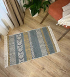 Patterned gray and yellow rug on a wooden floor with a plant and chair in the background