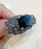 A navy blue stone ring with silver marcasite details, held in a person's hand.
