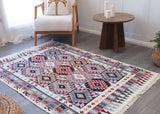 Patterned very large Armenian rug with traditional ornaments in blue and red  on a wooden floor with a chair and side table in the background