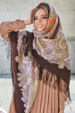 A Slavic blond woman wearing a brown and orange merino wool scarf with a geometric and herbal pattern and silky fringe.