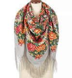 Floral patterned scarf with fringes on a mannequin against a white background. The intricate Slavic traditional design features layers of bright red and orange peony blossoms, slate blue floral clusters, and a delicate gray frame, perfectly accentuating a classy winter fashion accessory.