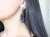 A set of sterling silver jewelry featuring purple topaz stones, including a ring and long earrings with marcasite designs on a black haired woman`s ear.