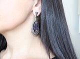A sterling silver very long  earrings with a purple topaz centerpiece, surrounded by marcasite accents, displayed on a ear to show size.