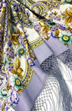 Close-up of a floral-patterned fringed shawl with a purple flowers and tassel.