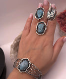 Hand wearing natural gemstone handmade jewelry set ring, earrings and bracelet with blue stone on a neutral background