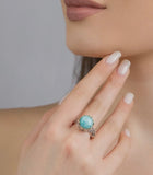 Close-up of a hand wearing a ring with a blue larimar gemstone against a neutral background