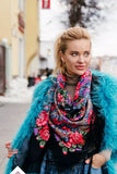 Woman wearing a colorful floral scarf in blue and red and blue fur jacket in an urban setting. She wear a black large shawl with red vintage roses which look very contemporary and fashionable.