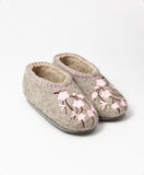 A pair of handmade felt house slippers in a warm taupe-gray color, decorated with pink embroidered cherry blossoms and dark brown stems on the toe area.