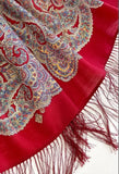 Red shawl with intricate paisley patterns and fringes on a red background