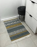 Patterned gray and yellow rug on a tiled floor with a black stool and white cabinet in the background.