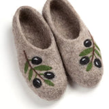 A pair of felted wool slip-on slippers in a warm taupe-brown color, decorated with green leaves and black embroidered olives on the side, shown on a white background.