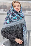 A woman wearing a large shawl on her head in gray with large vintage sky blue peony flowers. The material is wool with silky fringe.