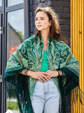 Woman wearing a green patterned shawl outdoors. This green shawl with yellow design has deep, rich colors. A woman wearing it enjoys a classic and polished look.