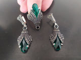 Very long silver earrings with green emerald and black marcasite stones, held in a person's hand.
