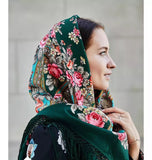 Woman wearing a floral headscarf. A soft sea-green merino wool shawl with turquoise and teal accents, decorated with pink vintage peony flowers. Oversized and warm, it wraps beautifully around the shoulders and adds a timeless, feminine touch.
