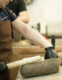 A pictures shows how woolen slippers are handmade and handwoven. The picture shows the process, the man with a wooden stick making a handwoven slipper.