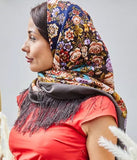 A woman wearing an authentic brown merino wool shawl adorned with beige and navy blue ornaments and floral details. The design reflects timeless elegance, finished with a silky fringe that moves beautifully. Warm, refined, and crafted from premium merino wool, this shawl is perfect for both everyday wear and special occasions.
