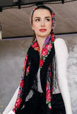 Woman wearing a black floral headscarf. The  scarf is black with large red roses on it in vintage style. The scarf has a high quality and made of merino wool and silky fringe.
