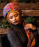 Woman wearing a colorful headscarf and patterned shawl in a rustic setting. The material is merino wool.