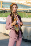 Woman in a pink outfit with a colorful scarf standing outdoors.