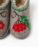 Close-up of a pair of felt 100%  woolen slipper shoes in a warm gray-brown tone, decorated with embroidered green leaves, red berries, and black branches.