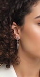 Close-up of a person with styled hair and small cross stud earrings against a blurred background