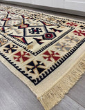 A traditional Eastern-style area rug with a cream base and geometric patterns in black, red, and beige, shown laid out on a gray wood floor.