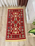 A rectangular red area rug with a traditional Armenian geometric tribal pattern in beige, black, and white, featuring gold fringe on the top and bottom, shown on a light wood floor.