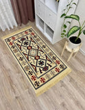 A rectangular woven Armenian runner rug with a geometric tribal pattern in beige, black, red, and brown, featuring fringe on the ends, shown on a light wood floor in a room setting next to a white cabinet and a potted plant.
