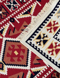 Close-up of a patterned rug with geometric Armenian-style motifs in red, cream, black, and tan, showing fringe along one edge.