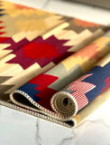 A close-up of a folded and rolled area rug with a Armenian geometric pattern in red, navy blue, beige, and brown, resting on a white marble surface.