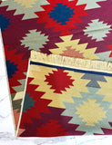 A folded woven area Armenian rug with a Southwestern geometric pattern in red, navy blue, beige, and dusty pink, displayed on a white marble surface.
