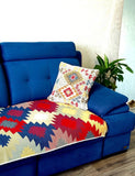 A vibrant blue upholstered sofa in a living room setting, styled with a colorful geometric patterned throw blanket and a matching decorative throw pillow.