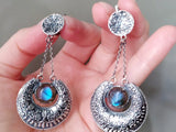 Armenian handmade Silver earrings with blue pearly gemstones held in a hand against a neutral background