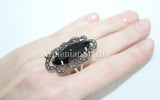 Black ring with intricate design on a hand against a white background