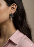 Close-up of a woman wearing an flower earring with a pearl on a neutral background