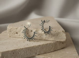 Pair of Armenian handmade silver hoop earrings with rays  on a textured stone surface with a blurred background
