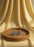 Silver Armenian coat of arms earrings with pearls on a woven tray against a yellow curtain