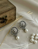 Silver earrings with pearls on a textured surface with feathers and a wooden box.
