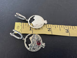Earrings pomegranate and Ararat silver with circular designs and a central gemstone on a black background with a ruler for scale.