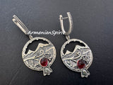 Silver earrings with circular pomegranate designs and red gemstones on a dark background with Ararat mountain and grape Armenian ornaments.